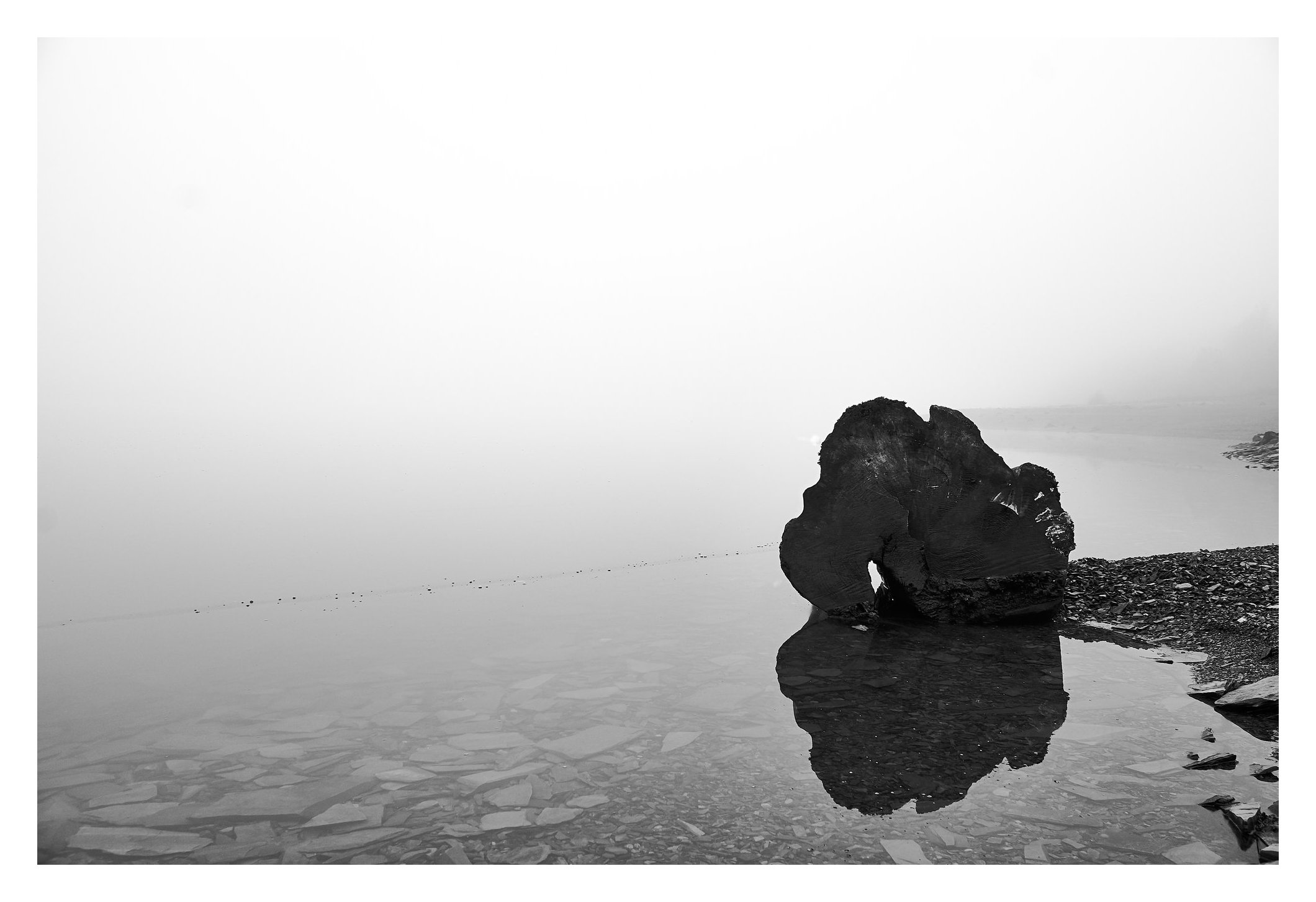 Ein dunkler Fels spiegelt sich in stillem Wasser